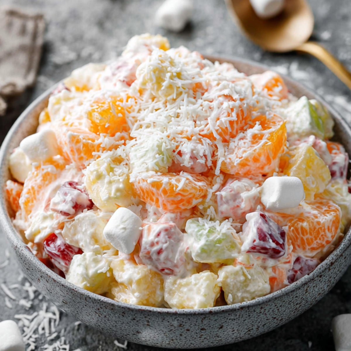 ambrosia fruit salad Finished ambrosia salad served in a gray ceramic bowl, creamy fruit salad with mandarin oranges, pineapple, cherries, coconut, and mini marshmallows, styled food photography, soft daylight, textured stone background, scattered marshmallows, professional food blog look, ultra realistic”