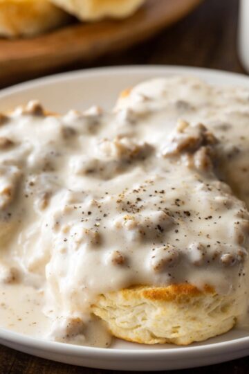 breakfast gravy recipe Fluffy homemade biscuits topped with creamy sausage gravy and black pepper, served on a white plate for a classic Southern breakfast.