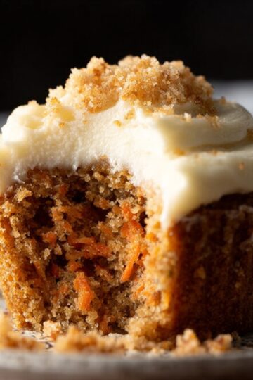 Easy Carrot Cupcake Recipe | Moist & Ready in 40 Minutes 21 carrot cupcake recipe A bitten carrot cake cupcake showing moist crumb texture inside, topped with thick cream cheese frosting, crumbs on plate, dramatic lighting, high-resolution dessert photography.
