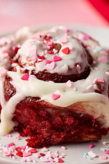 Best Red Velvet Cinnamon Rolls | Soft & Fluffy Recipe 19 red velvet cinnamon rolls Single red velvet cinnamon roll with cream cheese icing and heart sprinkles, cut open to show soft red interior.