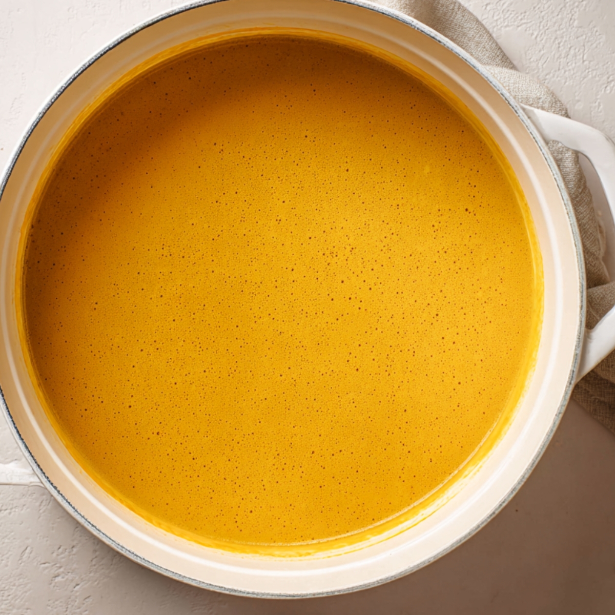 Italian Penicillin Soup Recipe 12 Overhead view of a large white pot filled with smooth golden vegetable soup, creamy texture and minimal styling on a light background
