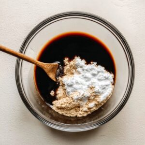 Easy Mongolian Ground Beef Noodles 14 Glass bowl with soy sauce, cornstarch, and brown sugar before mixing, flat lay food preparation on a light background.