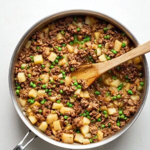 Easy baked beef empanadas | Golden & Freezer-Friendly 16 Ground beef empanada filling cooking in a stainless steel skillet with peas and diced potatoes, wooden spoon stirring, top-down view, clean white background, warm natural lighting, homemade comfort food, high-detail culinary photography