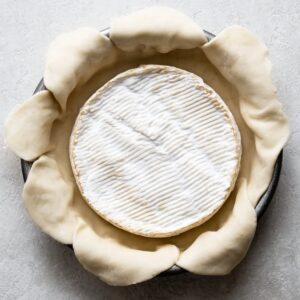 Easy Baked Brie in Puff Pastry Recipe 14 Wheel of brie cheese placed in puff pastry before baking in a round pan