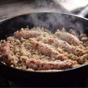 Breakfast Gravy Recipe 15 Breakfast sausage cooking in a cast iron skillet with steam rising, showing browned sausage links and crumbles.