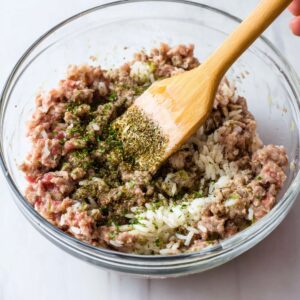 Cabbage Rolls Recipe 16 Close-up of ground meat, rice, and spices being mixed together in a glass mixing bowl.
