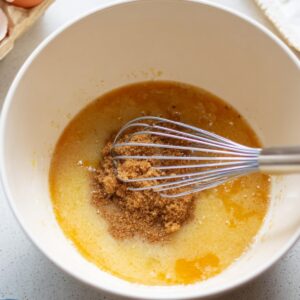 Easy Carrot Cupcake Recipe | Moist & Ready in 40 Minutes 16 Whisking eggs, brown sugar, and oil together in a large mixing bowl, baking ingredients visible around, natural daylight, overhead angle, step-by-step cake batter preparation.