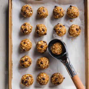Energy Ball Recipe | No-Bake Snack Ready in 10 Minutes 15 Top-down view of no-bake energy balls on a parchment-lined baking tray with a cookie scoop, step-by-step snack recipe