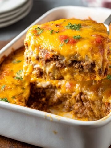 Golden, cheesy Cattle Drive Casserole being served, showcasing layers of ground beef, biscuits, and melted cheddar cheese topped with fresh herbs.