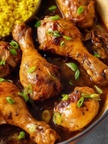 Drizzling sauce over tender Chicken Adobo, served with yellow rice and garnished with fresh herbs.